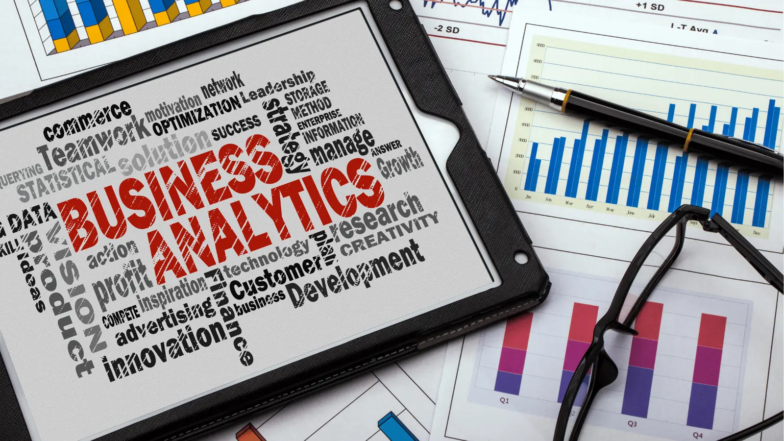 Tablet showing business analytics word cloud next to printed charts and glasses