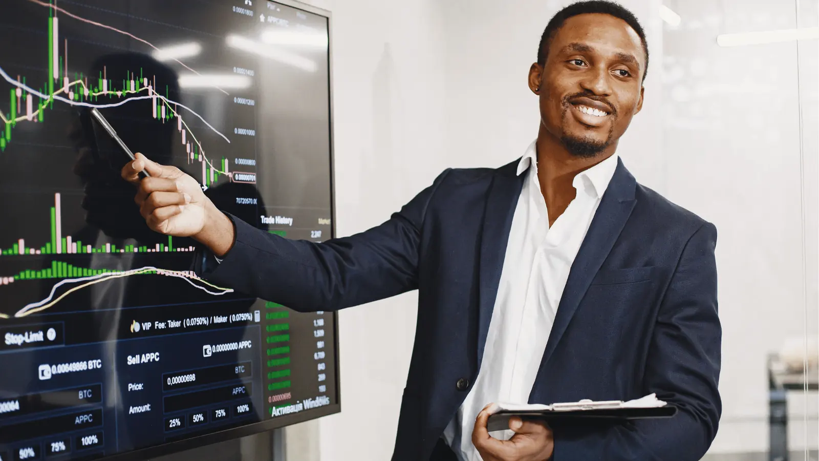 Smiling businessman pointing at large trading chart on screen holding a tablet