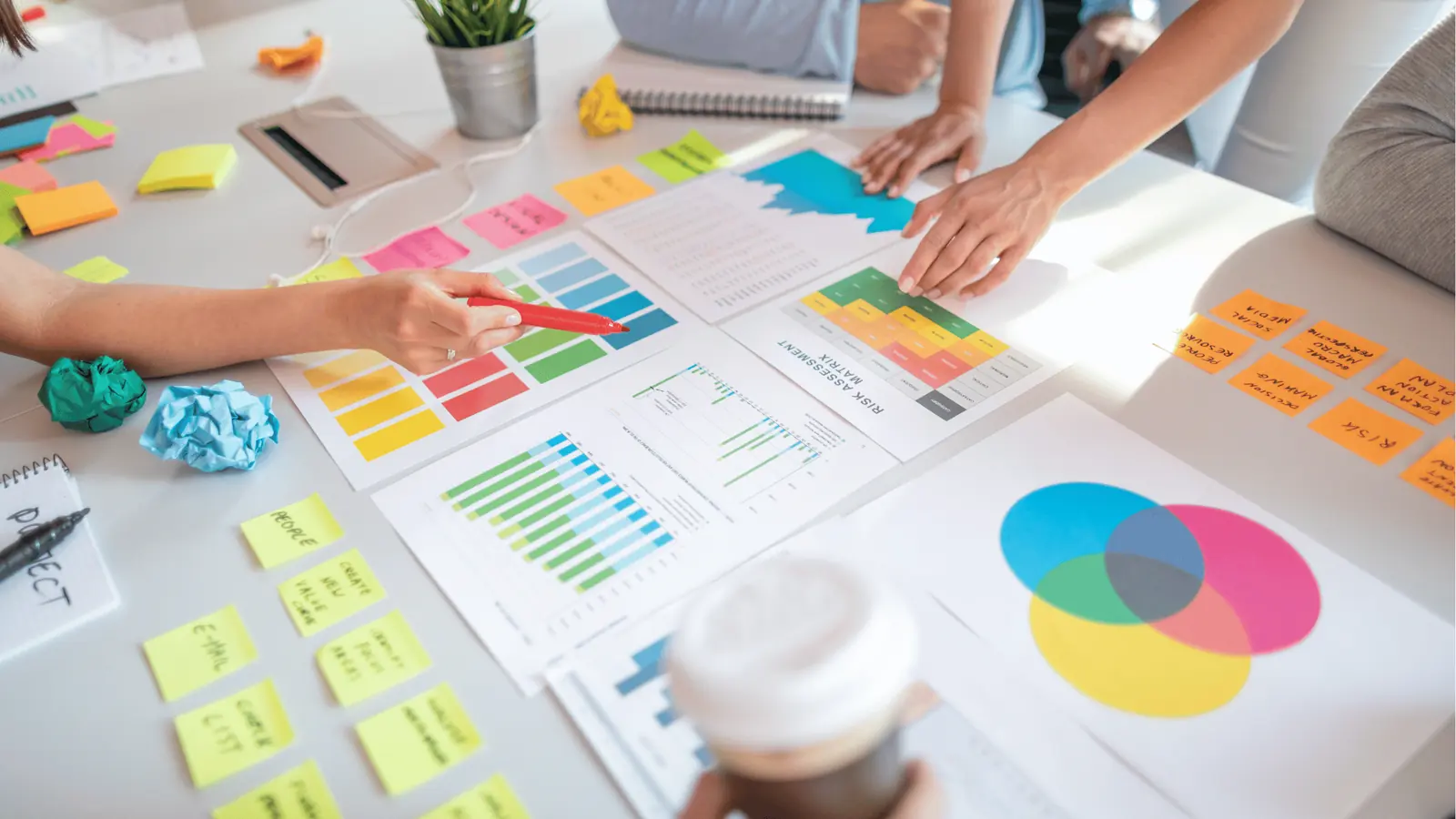Hands pointing at colorful charts, sticky notes, and a Venn diagram on a desk for brand management
