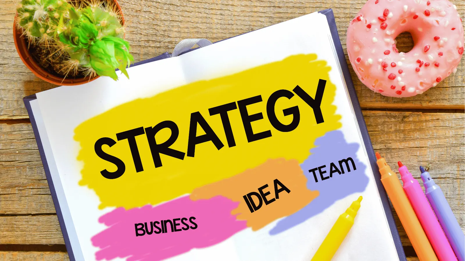 Open notebook with colorful strategy notes, markers, cactus, and pink donut