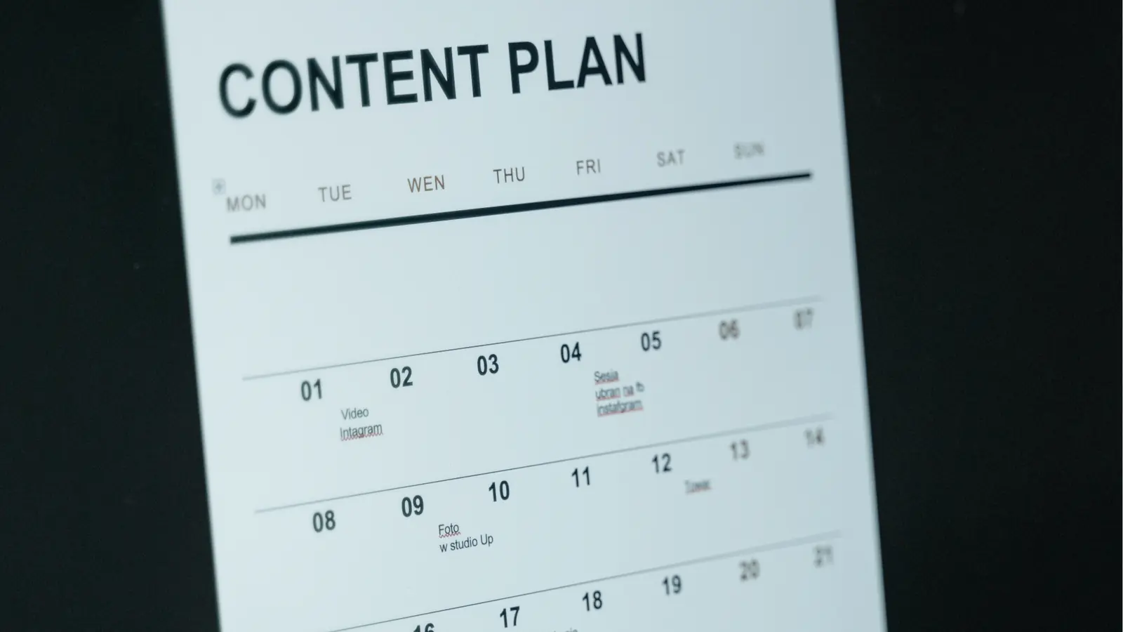 Tilted printed monthly content plan calendar page on dark background for campaign planning