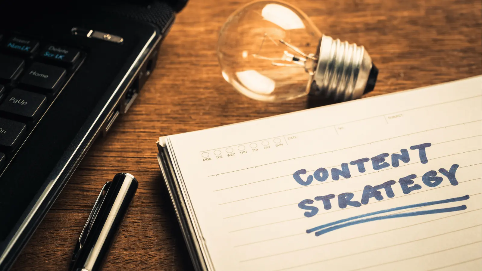 Notebook on wooden desk with handwritten 'Content Strategy' beside laptop