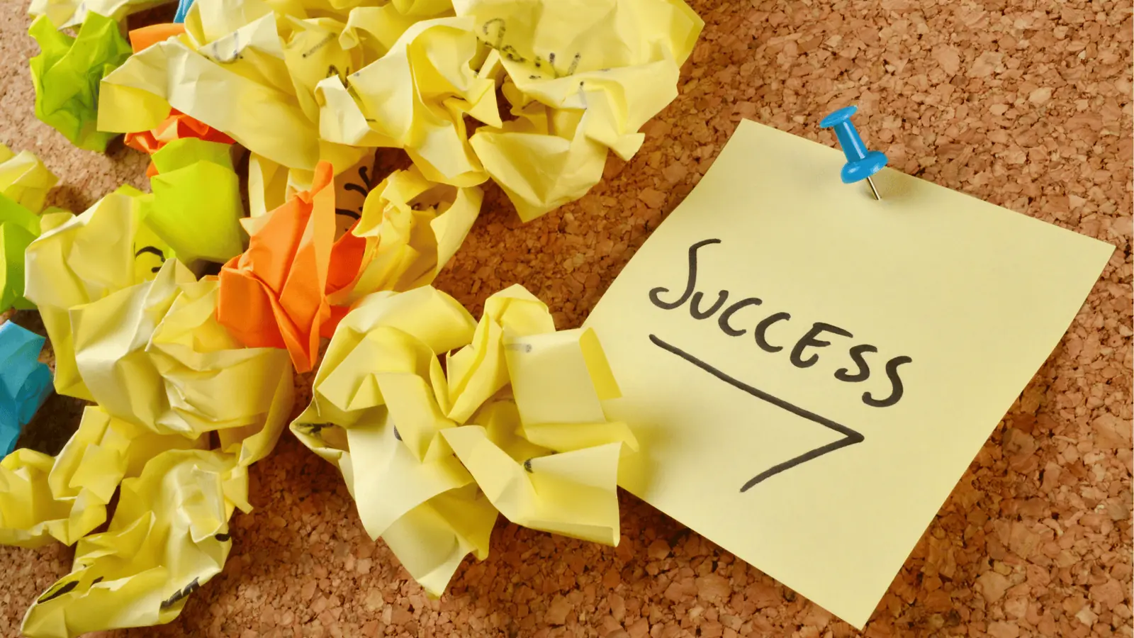 Yellow sticky note pinned to corkboard reading 'Success' beside crumpled paper