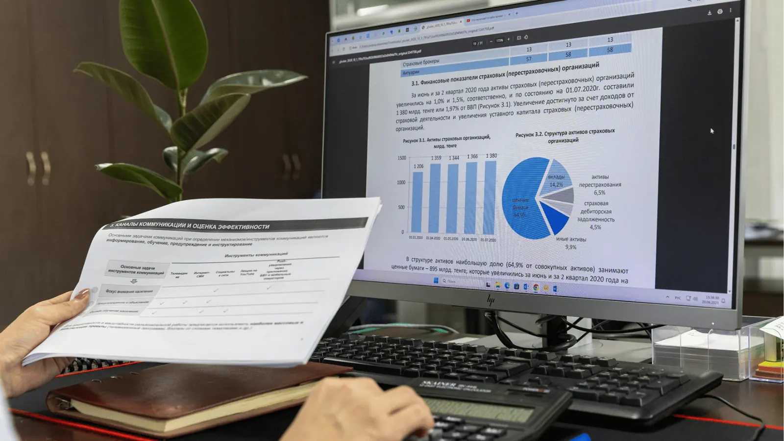 Hands holding printed report beside computer monitor showing bar and pie charts