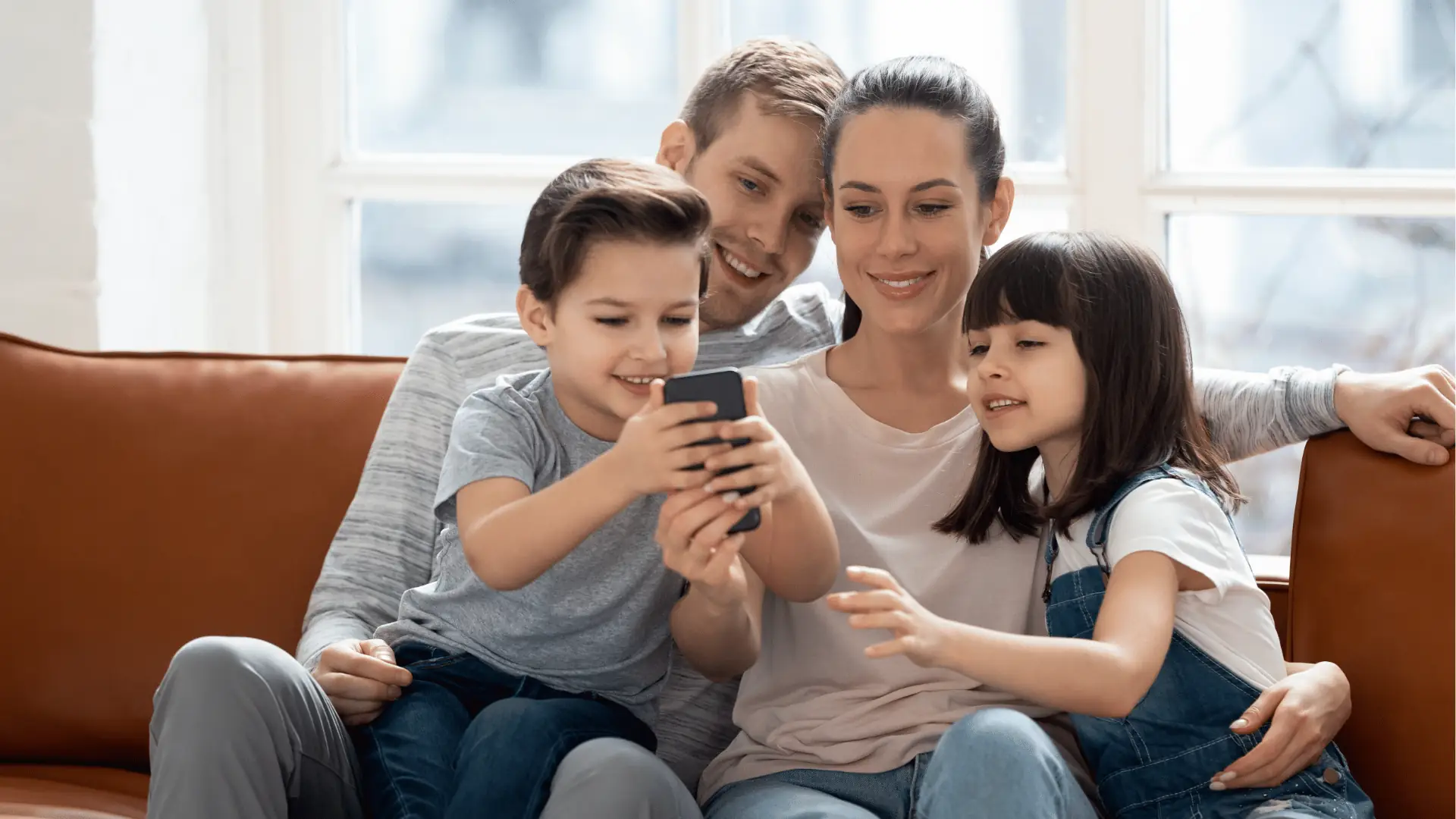 Family of four sitting on couch together looking at a smartphone screen