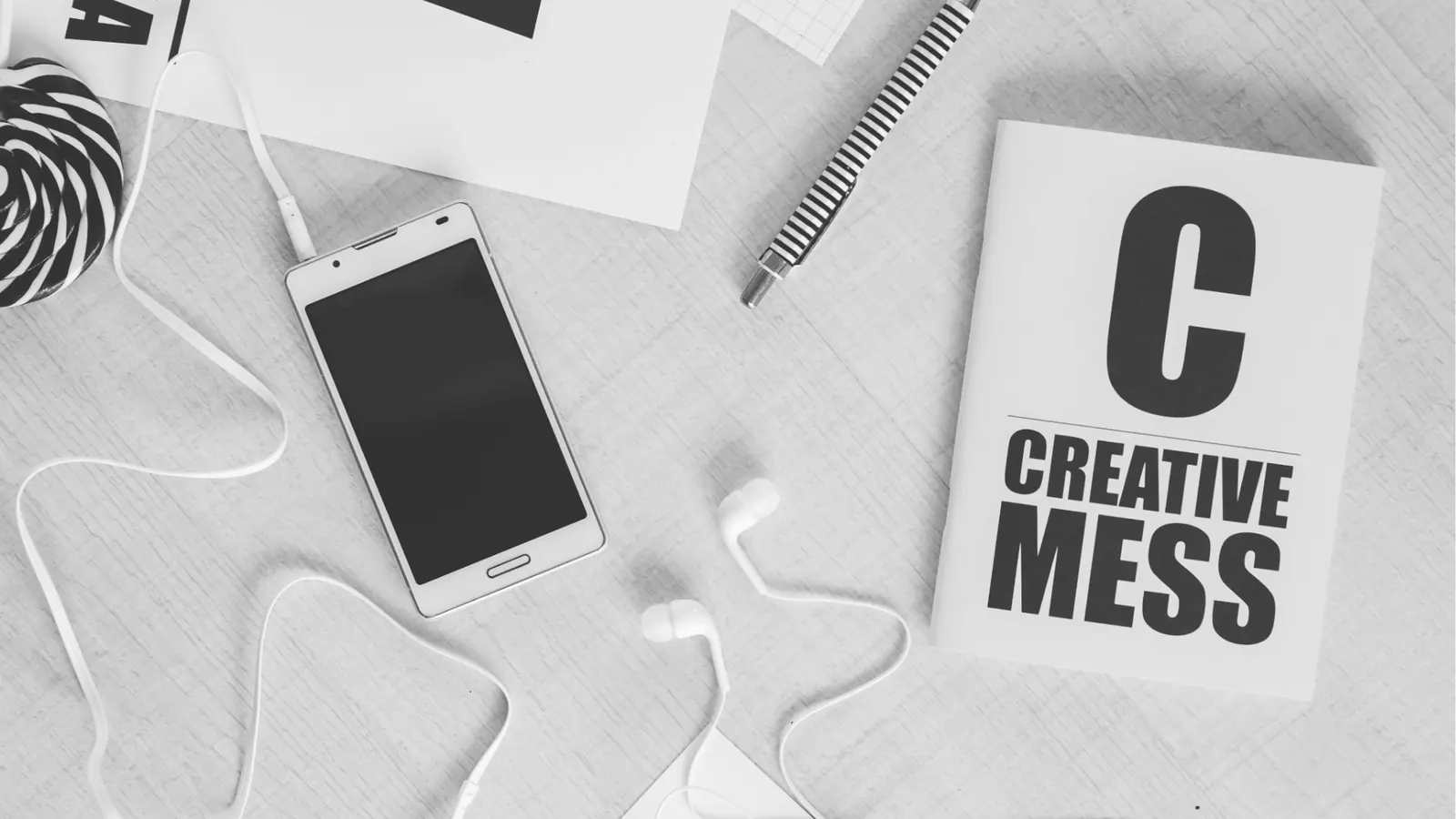 Top-down flat lay of smartphone, earbuds, pen and 'Creative Mess' notebook