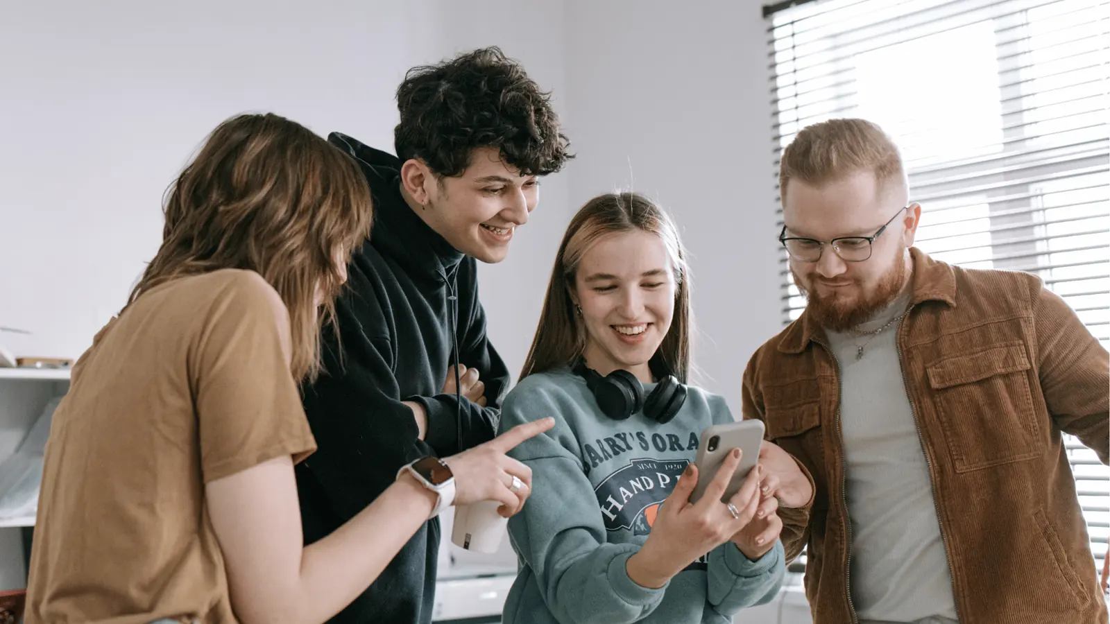 Four young adults smiling and looking at a smartphone screen together