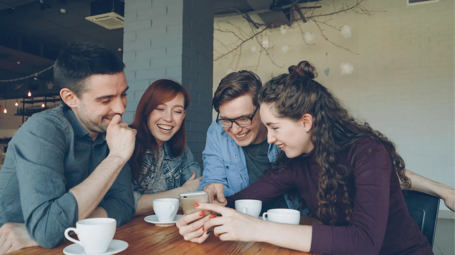 Teammates smiling over a phone in a cafe