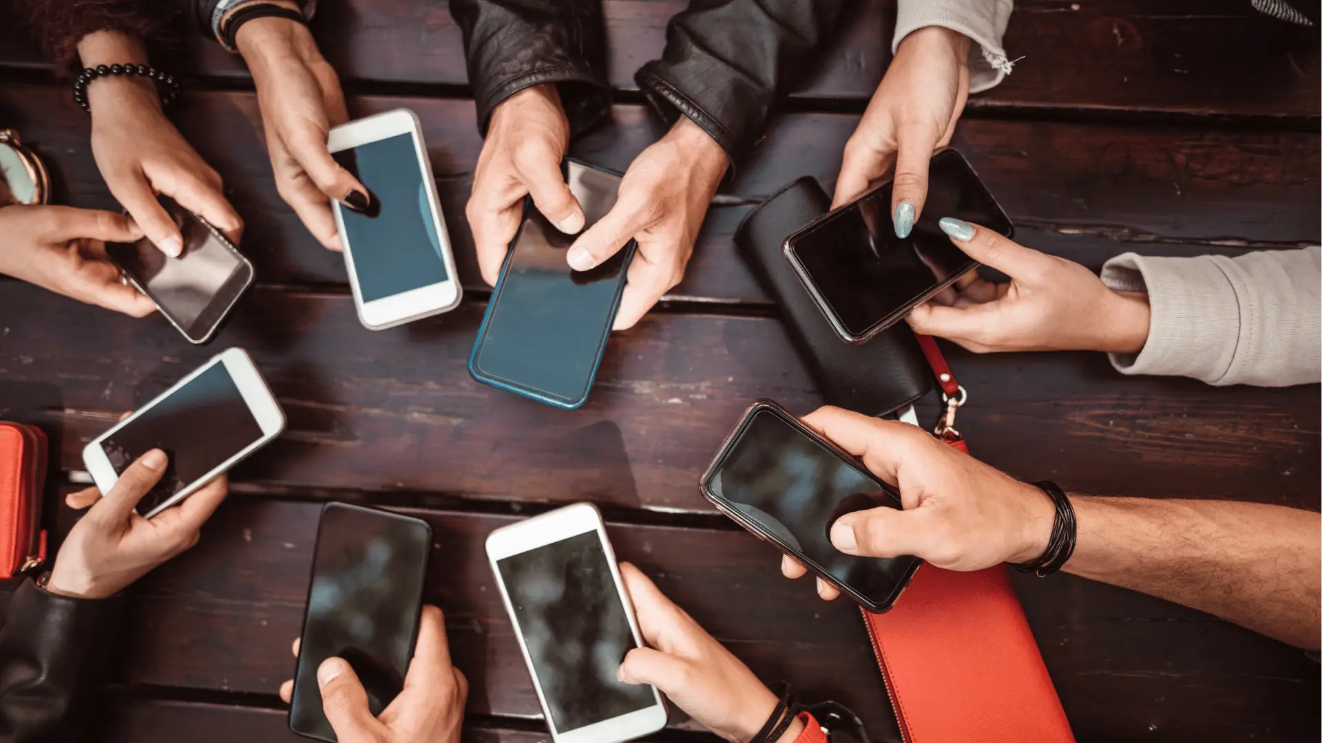 Overhead view of multiple hands holding smartphones on a wooden table