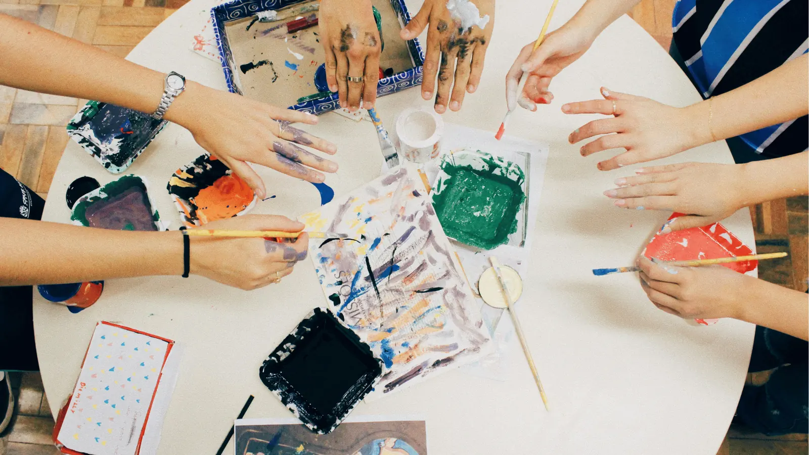 Overhead view of several hands painting with brushes and colorful paints