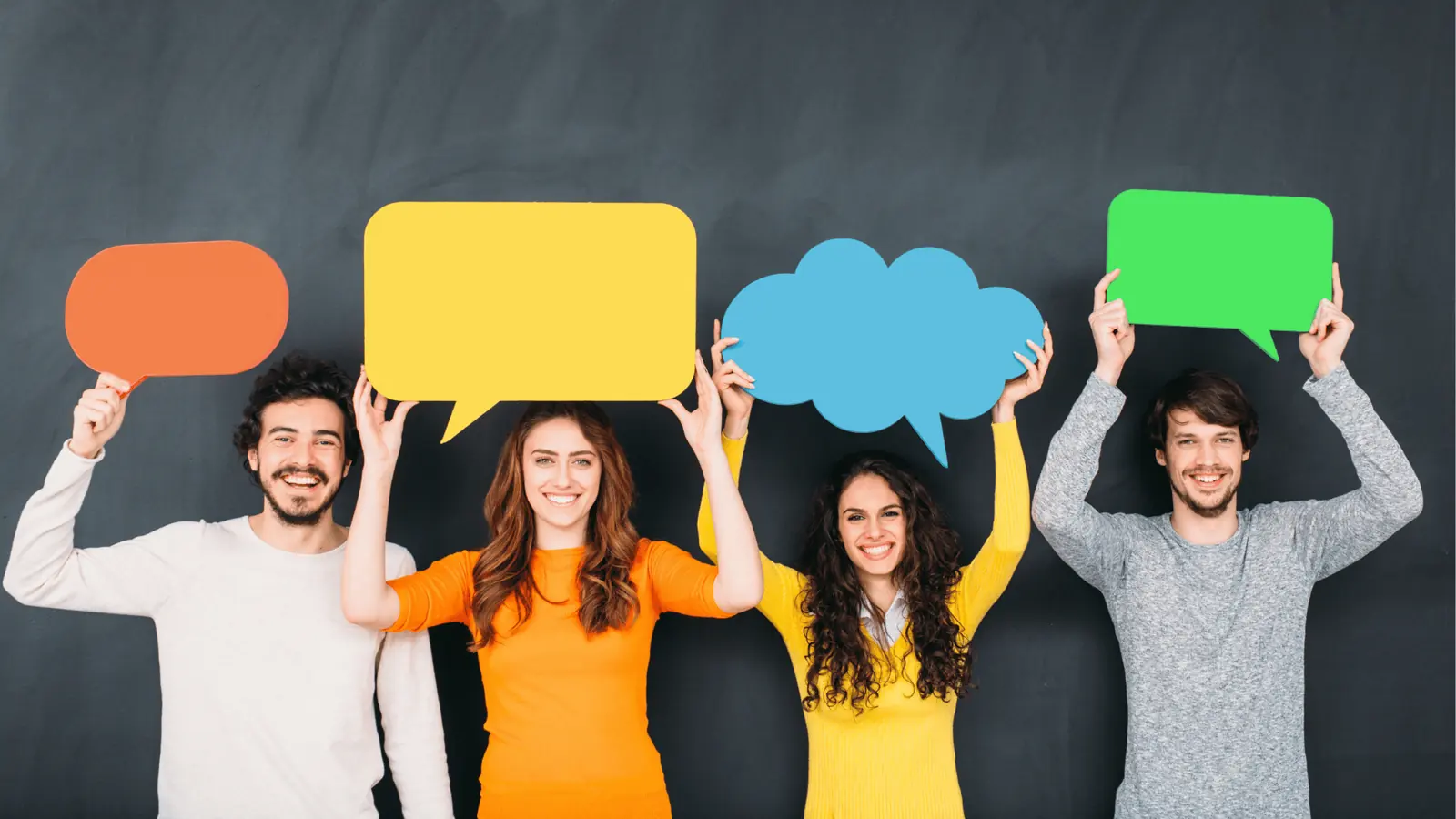 Four smiling people holding colorful speech bubble cutouts above their heads