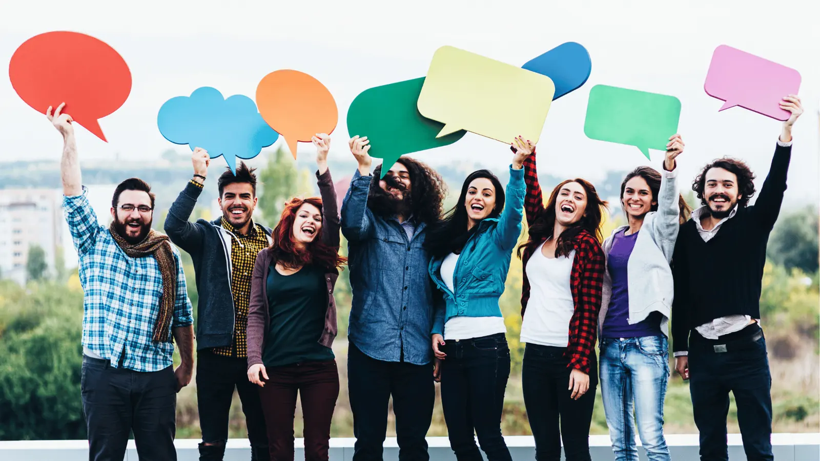 Diverse group of young adults holding colorful speech bubble signs outdoors for approval workflow