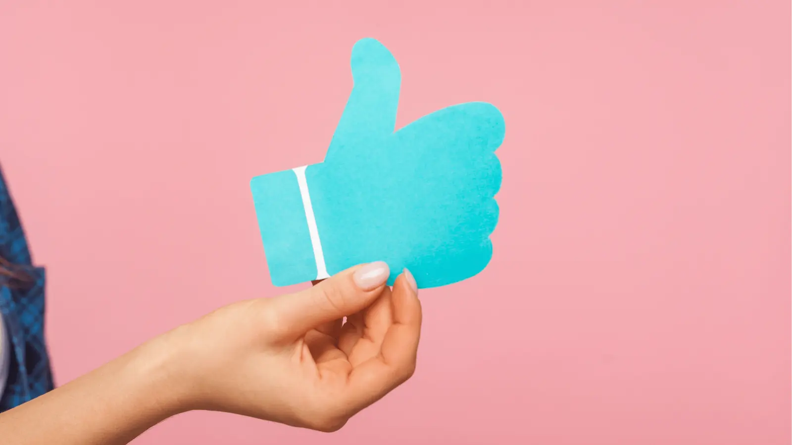Hand holding blue paper thumbs up cutout against pink background for asset management