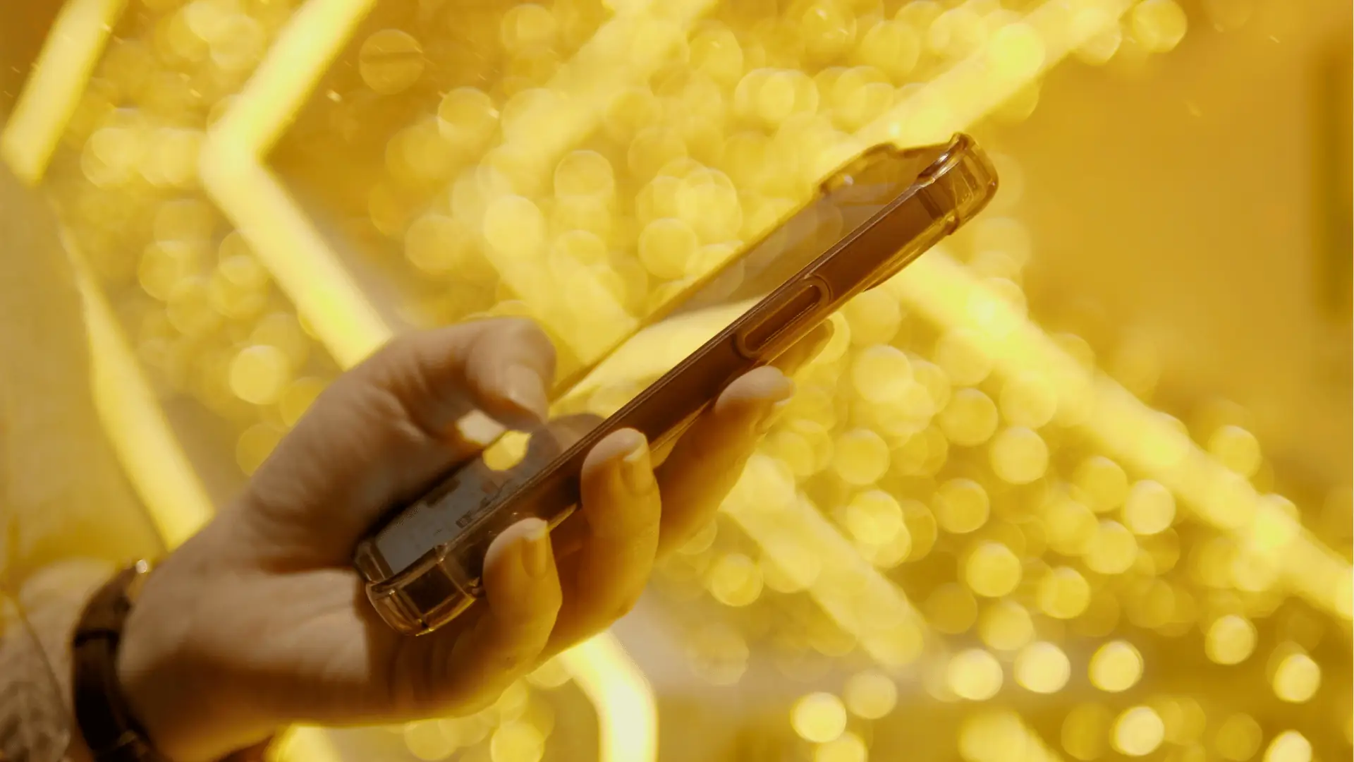 Hand holding smartphone with clear case against golden bokeh lights background