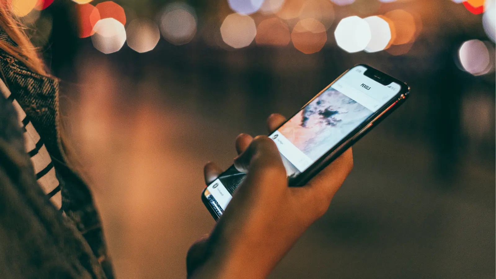Close-up of a hand holding a smartphone showing an image feed at night