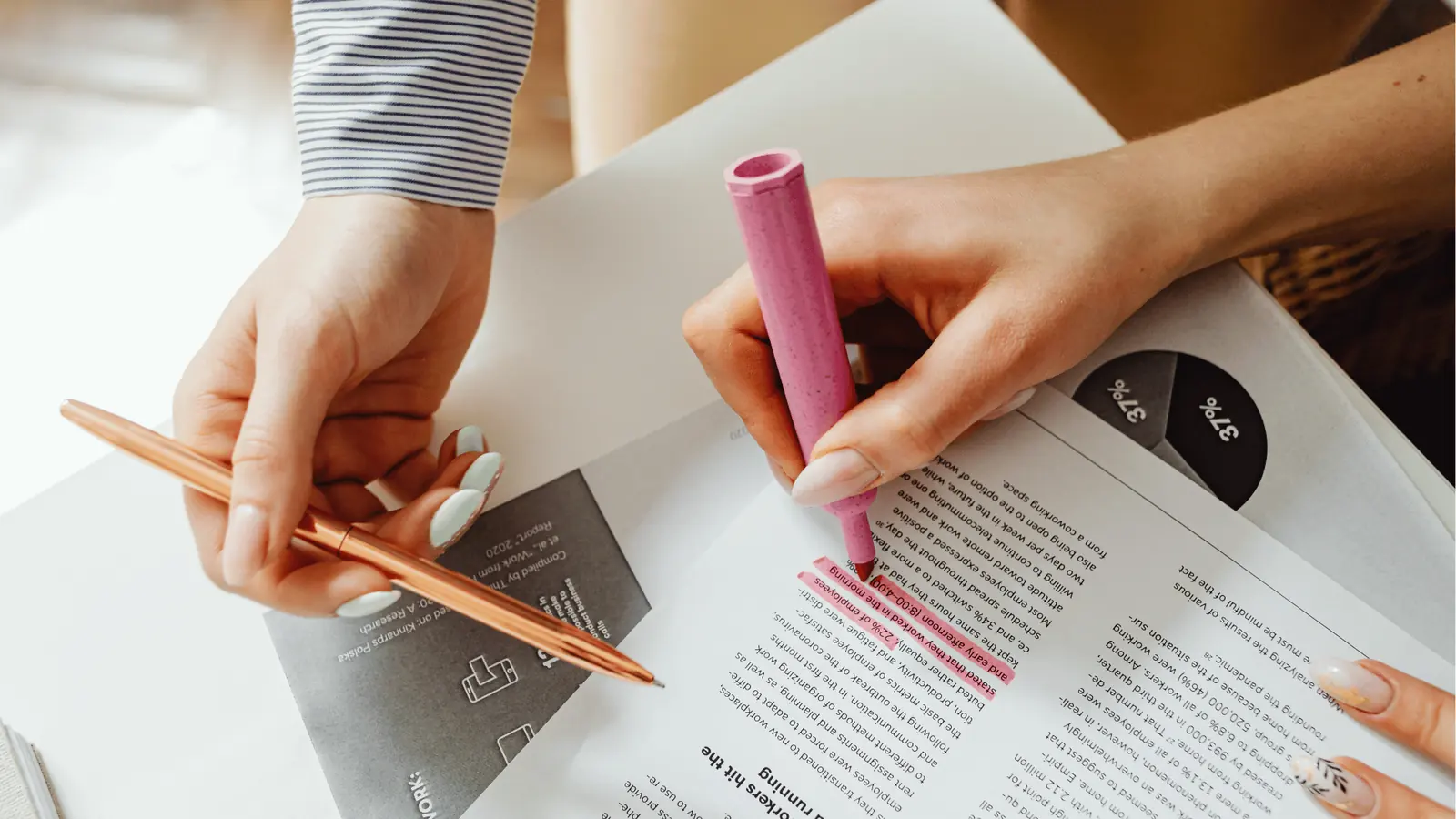 Two hands highlighting a printed report with a pink highlighter and holding a pen