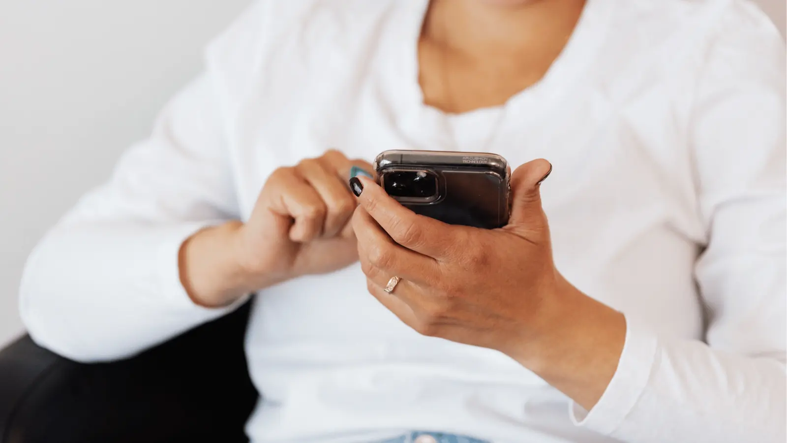 Close-up of hands holding smartphone and tapping screen while seated