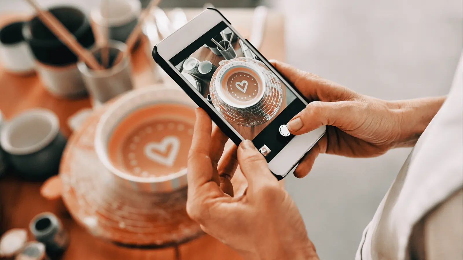 Hands holding smartphone photographing a decorated ceramic bowl with a painted heart