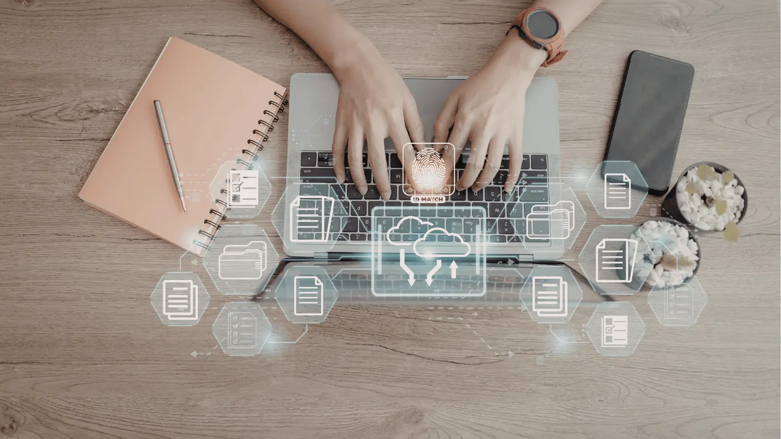 Top down view of hands typing on a laptop with cloud icons overlay for asset management