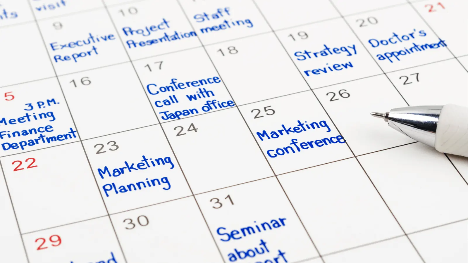 Close-up of paper calendar with blue handwritten meetings and a pen