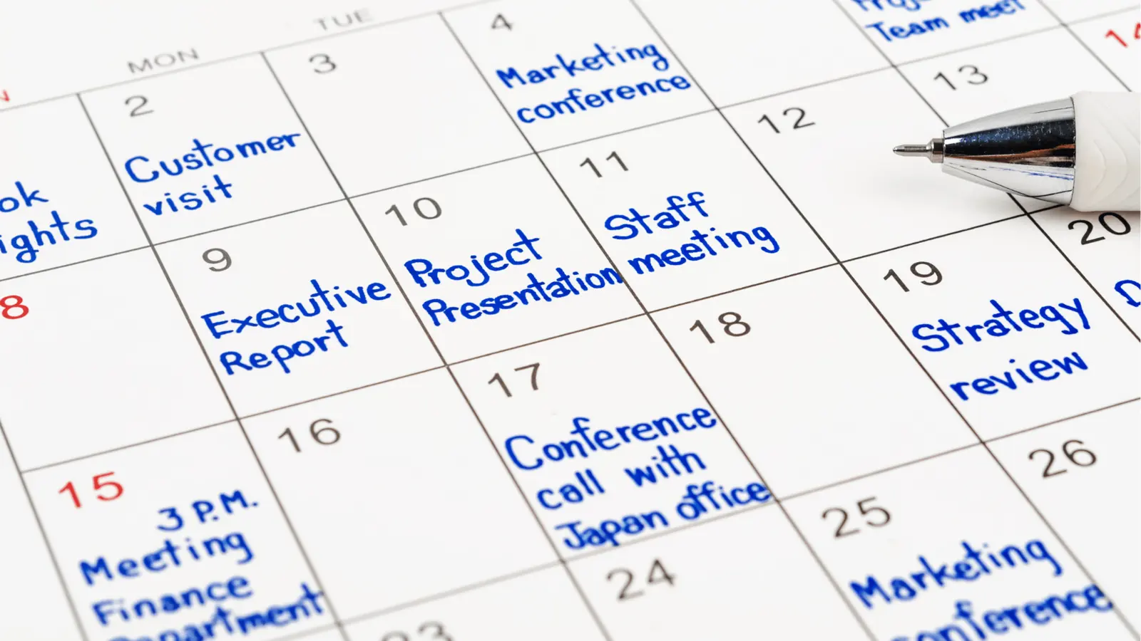 Close-up of calendar page with handwritten blue meeting entries and pen