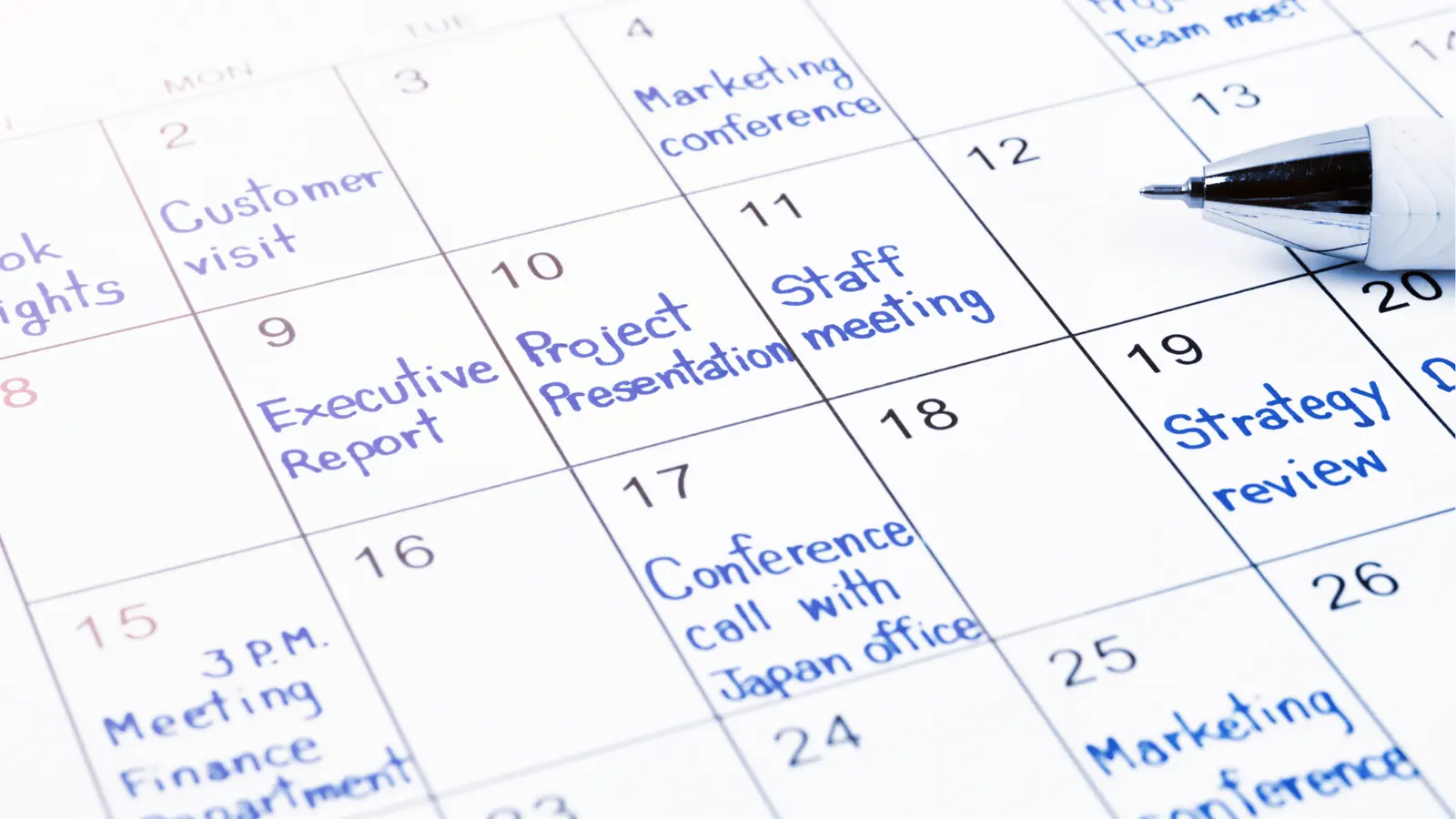 Close-up of monthly calendar with handwritten meetings and a pen for approval workflow