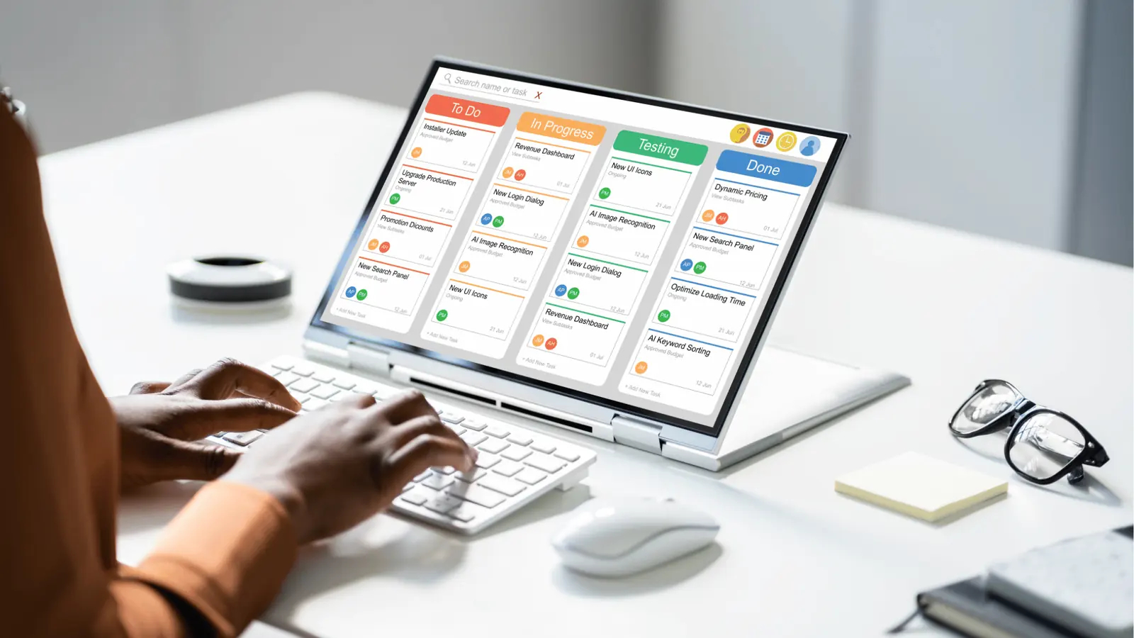 Hands typing by laptop showing a kanban task board with colored columns