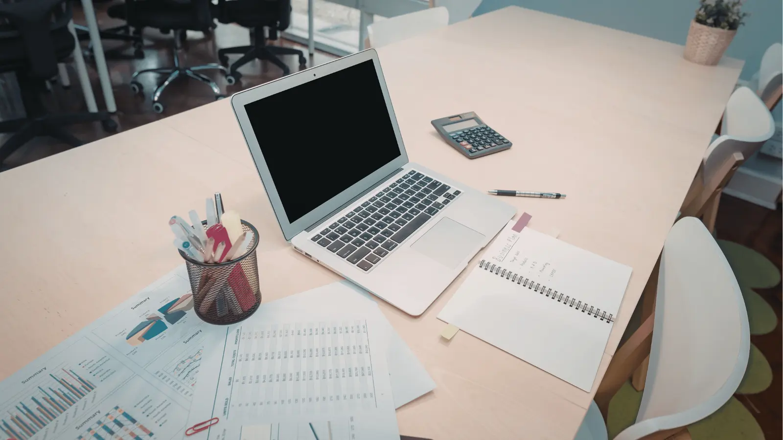 Silver laptop with blank screen surrounded by notebook, calculator, and charts