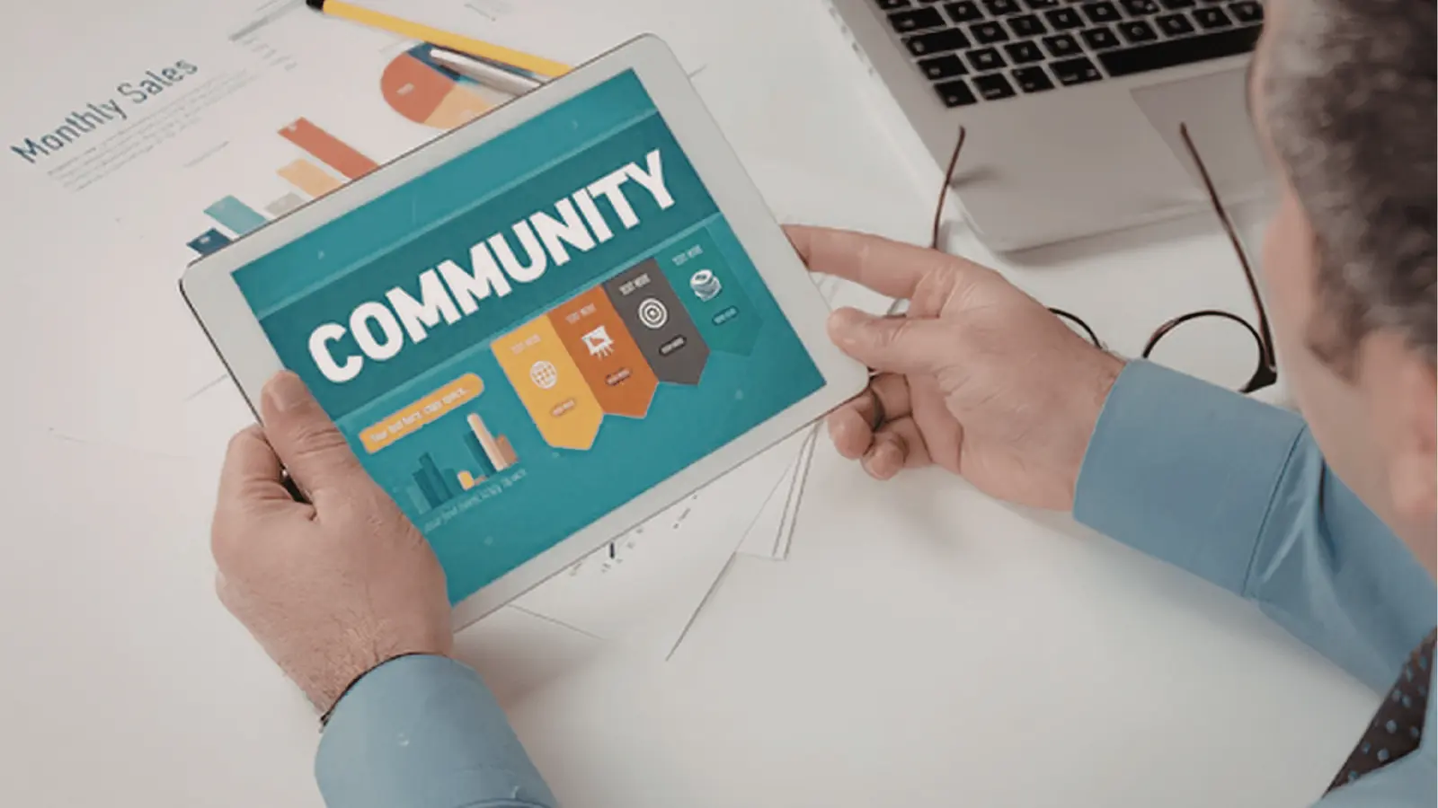 Man holding tablet that displays a teal COMMUNITY infographic at a desk for community management