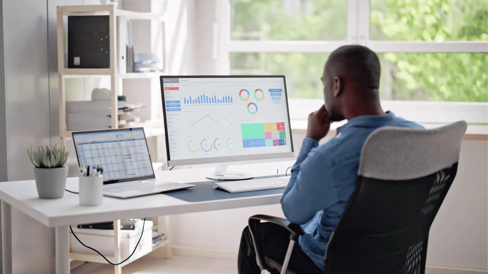 Man sitting at desk looking at analytics dashboards on dual monitors for creative production