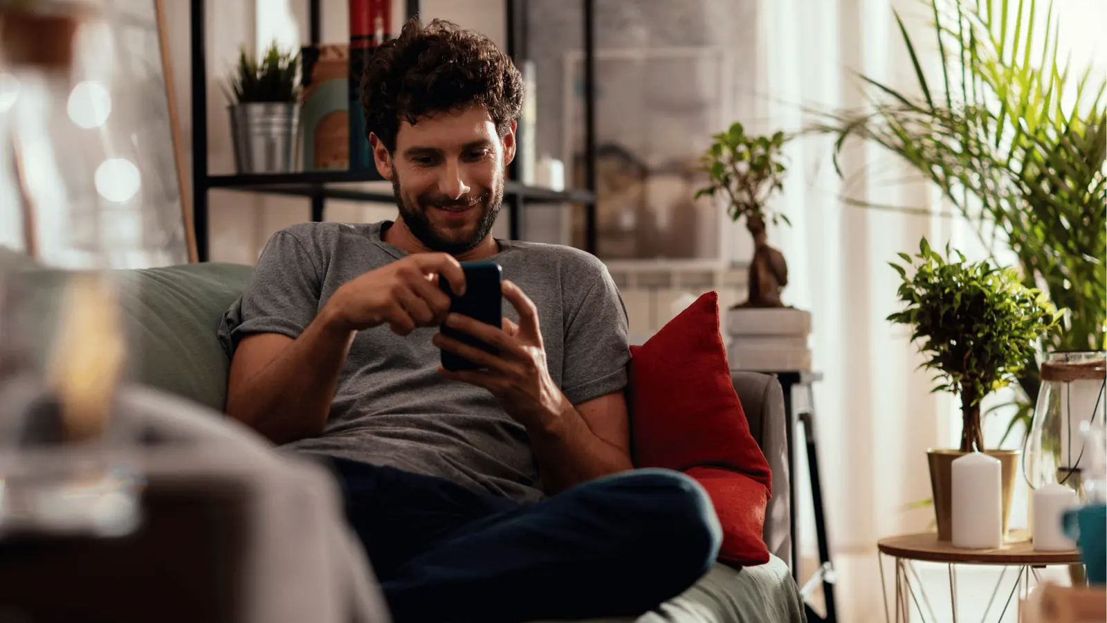 Smiling man lounging on couch and using a smartphone at home
