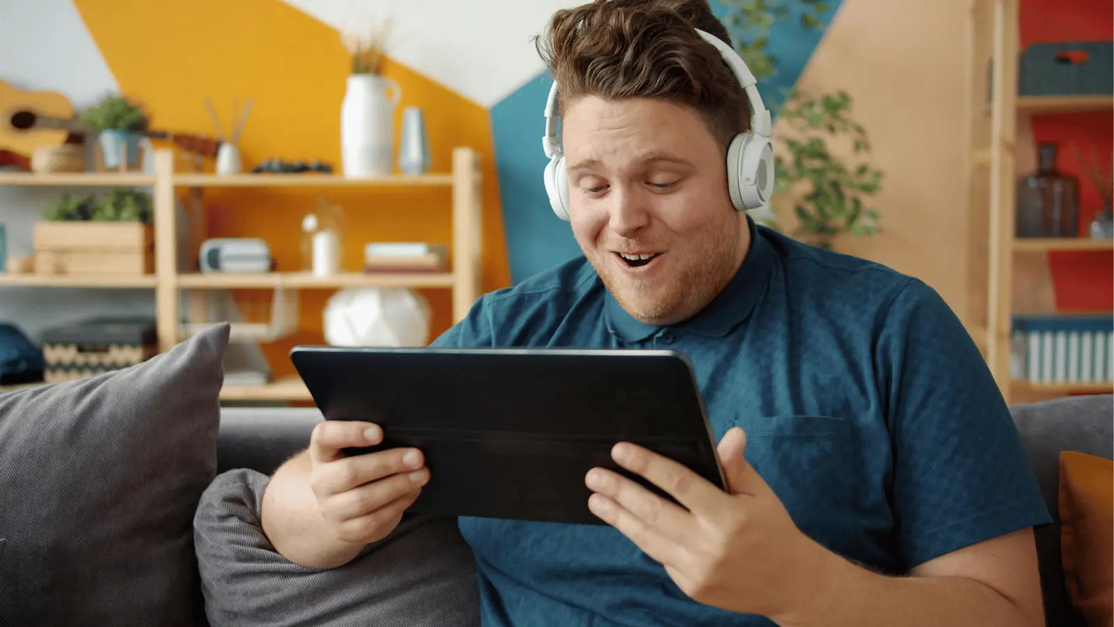 Man sitting on couch wearing headphones and smiling at tablet screen