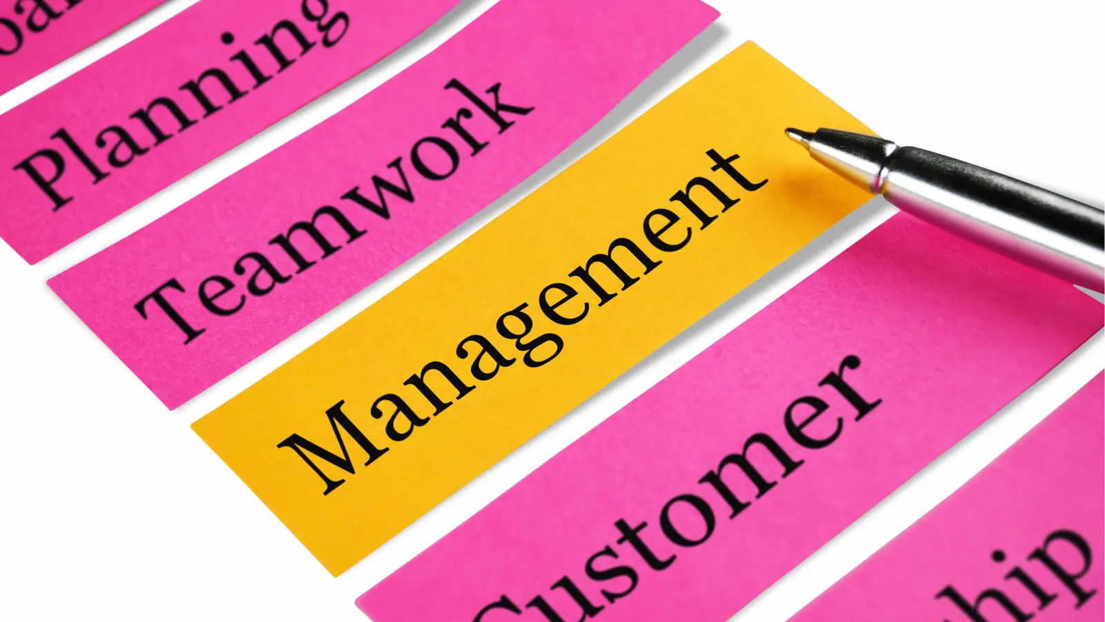 Close-up of yellow and pink paper labels with business words and silver pen