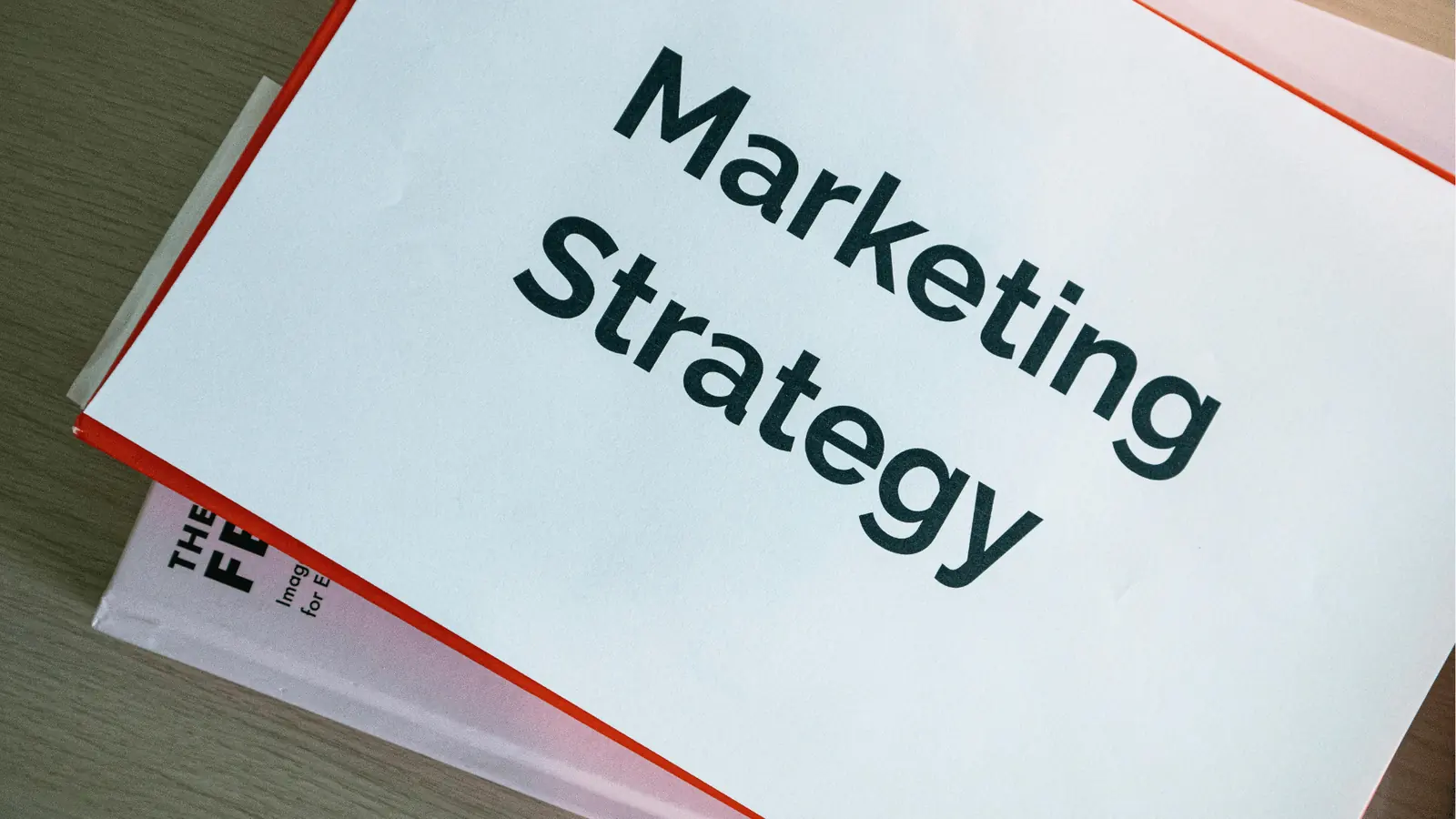 Booklet titled 'Marketing Strategy' lying on a wooden desk surface
