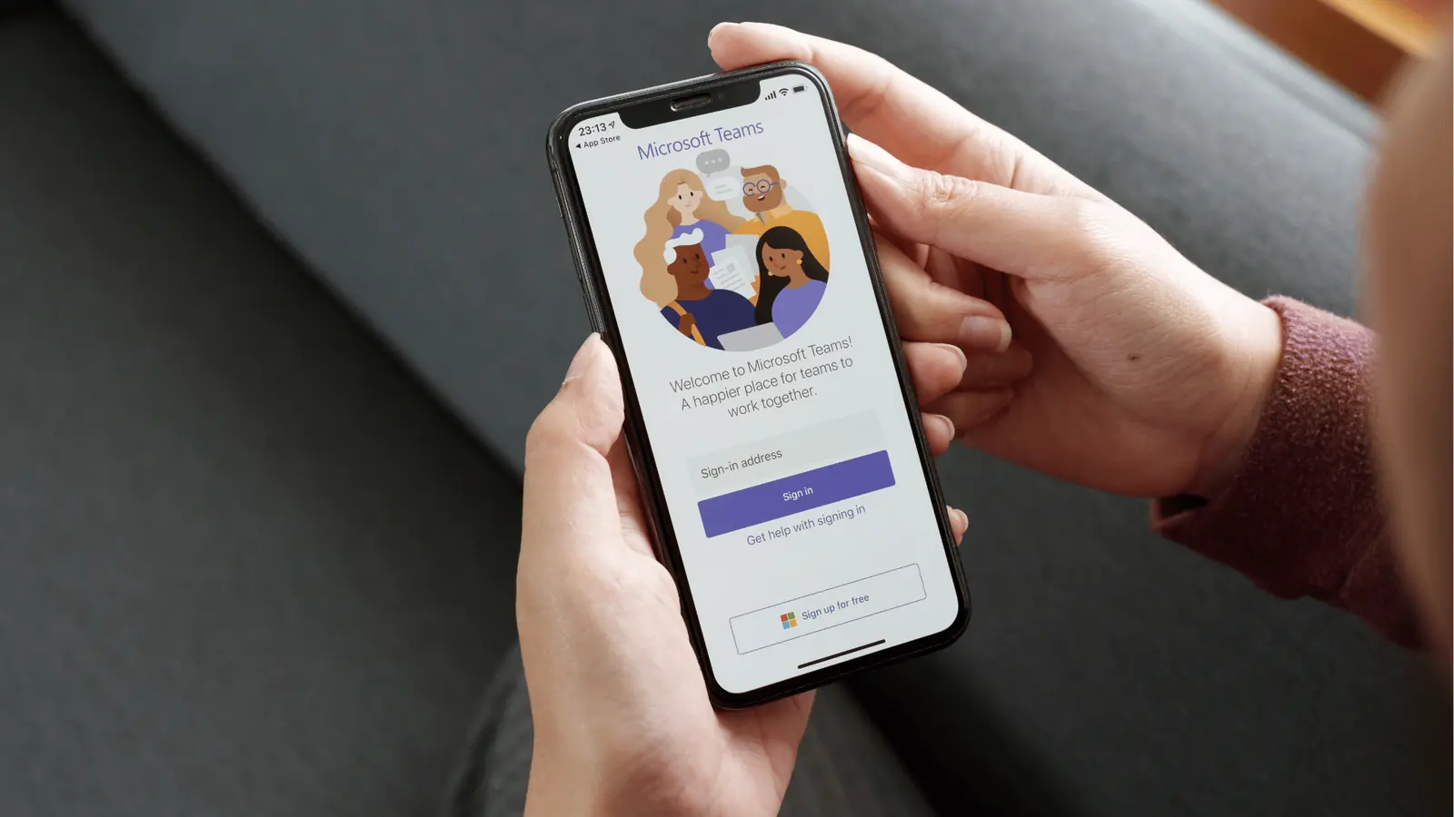 Hands holding smartphone showing Microsoft Teams sign-in screen on a couch
