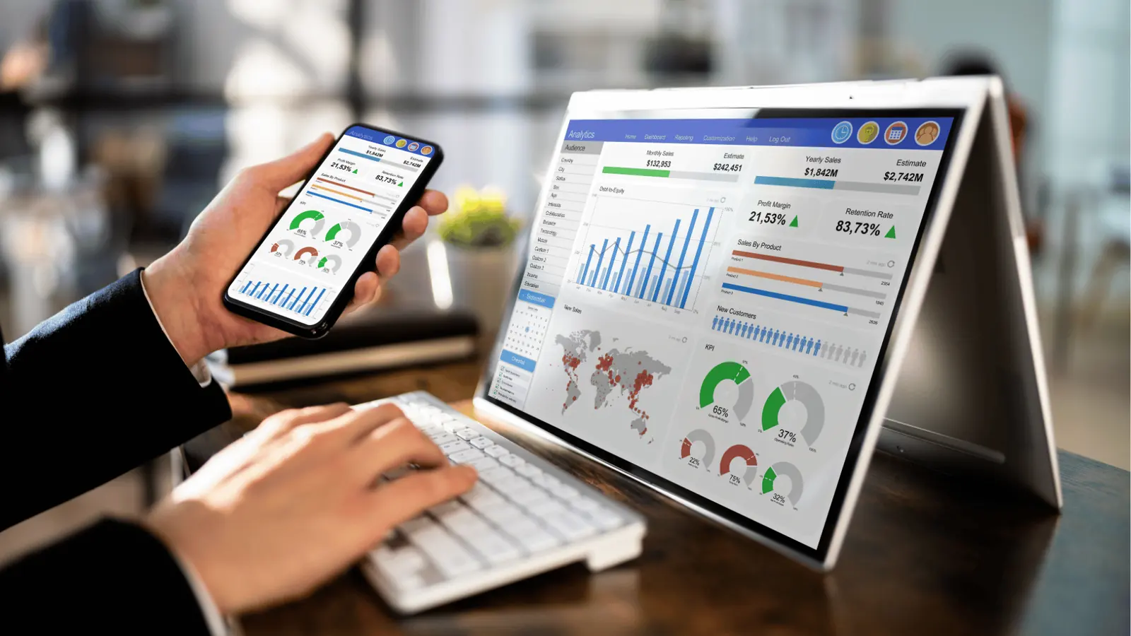 Person holding smartphone and typing on keyboard with analytics dashboard on tablet