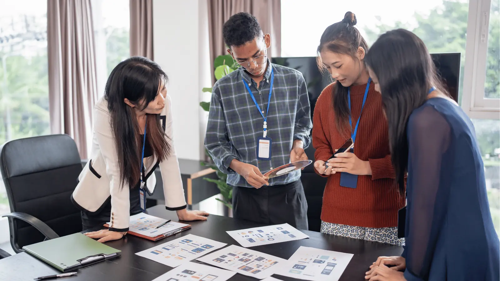 Four colleagues standing around table reviewing printed design mockups