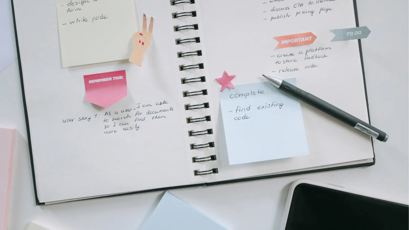 Open spiral notebook with sticky notes, pen, and handwritten task list