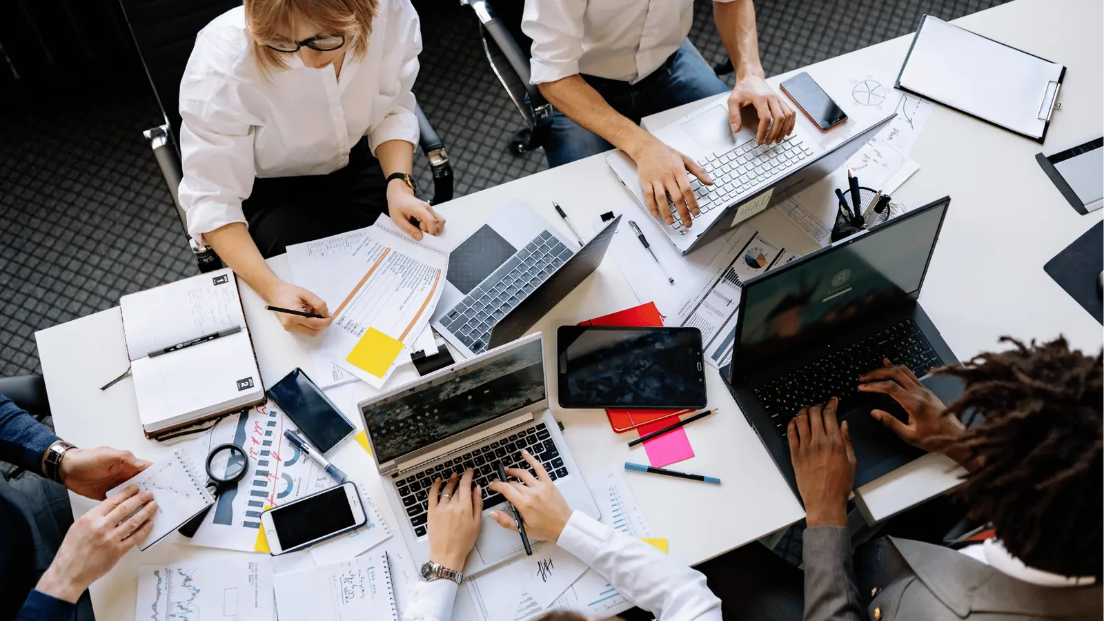 Overhead view of five people working at a cluttered office desk
