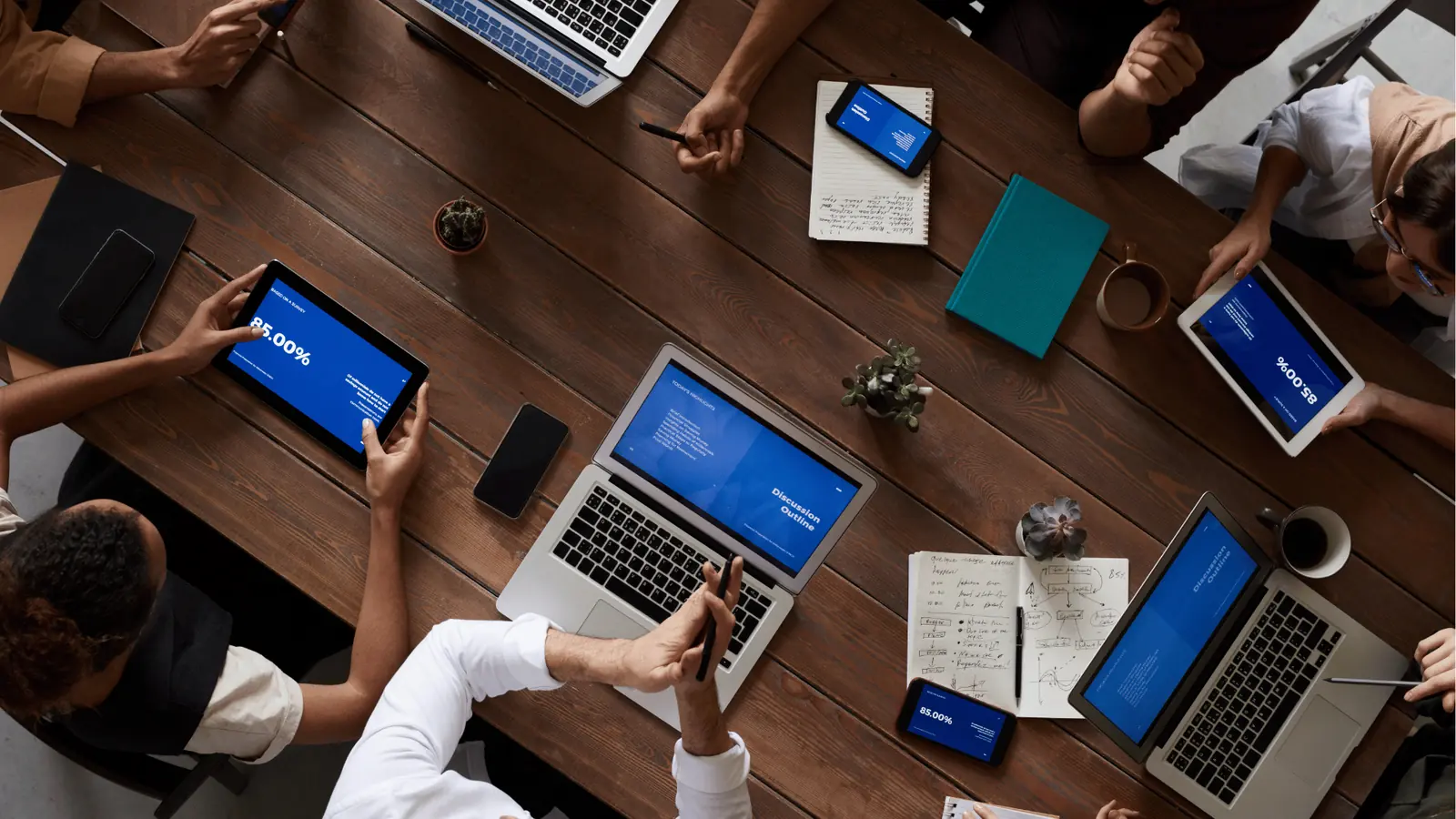 Overhead view of a team meeting with laptops, tablets, and notebooks on table for ROI reporting