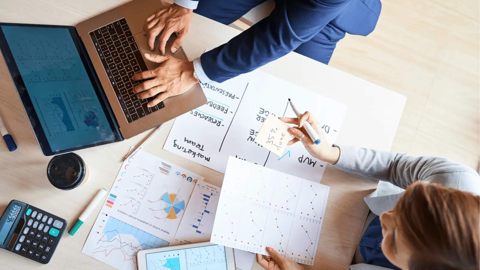 Overhead view of two people reviewing printed charts and a laptop for asset management