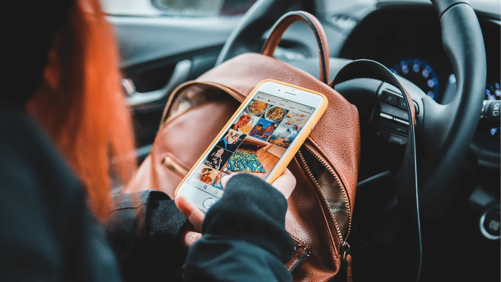 Person holding smartphone showing social media grid while sitting in a car