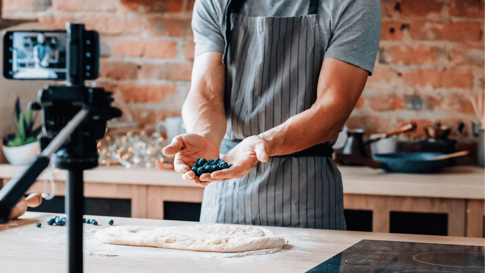 Person holding fresh blueberries over floured dough on a kitchen counter