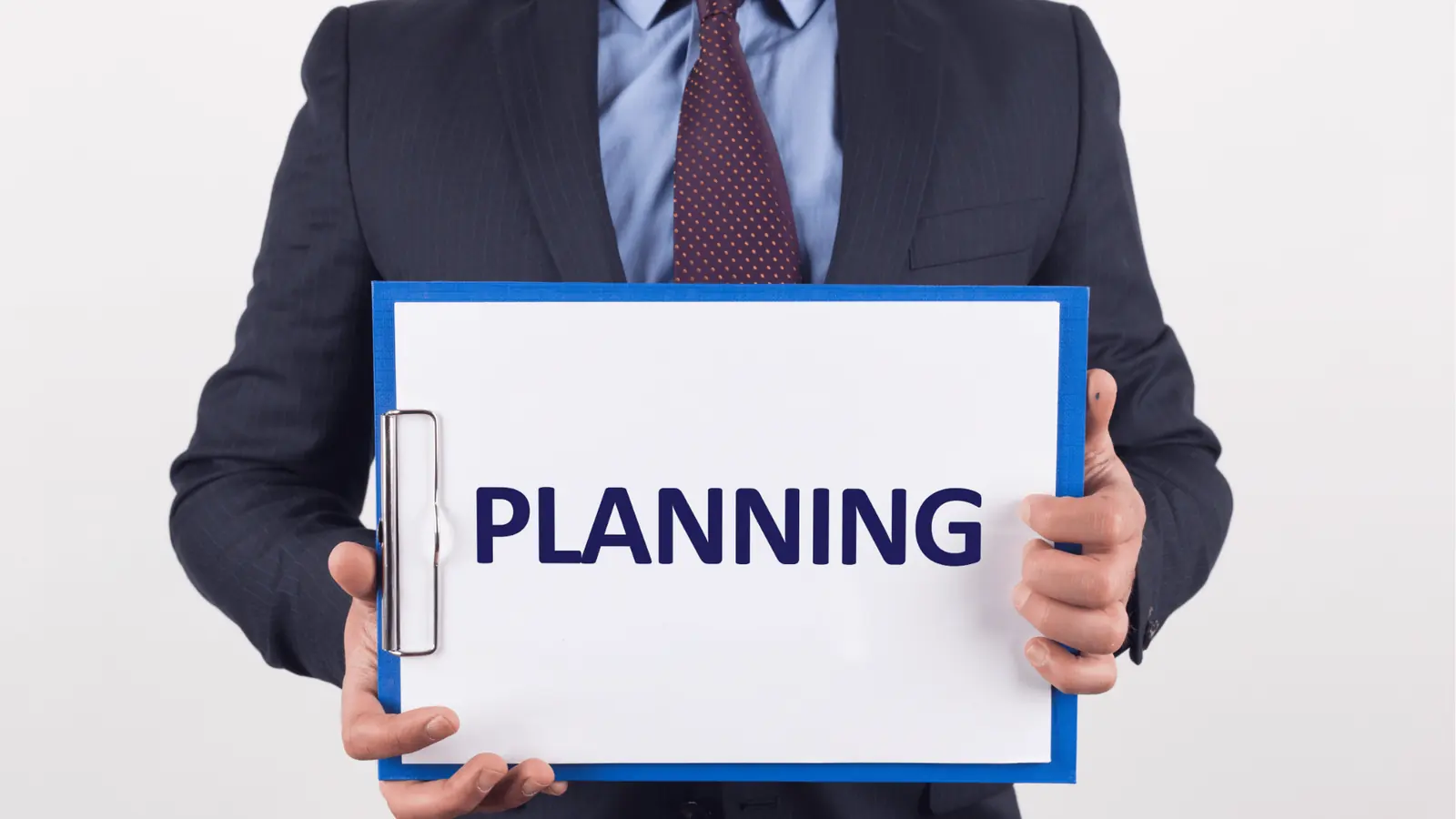 Person in a suit holds a clipboard with the word PLANNING in blue