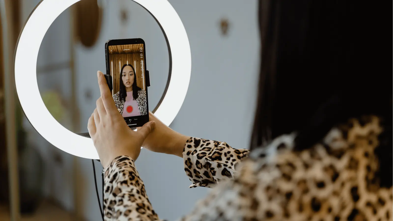 Person holding smartphone in ring light recording a selfie video wearing leopard print for scheduling