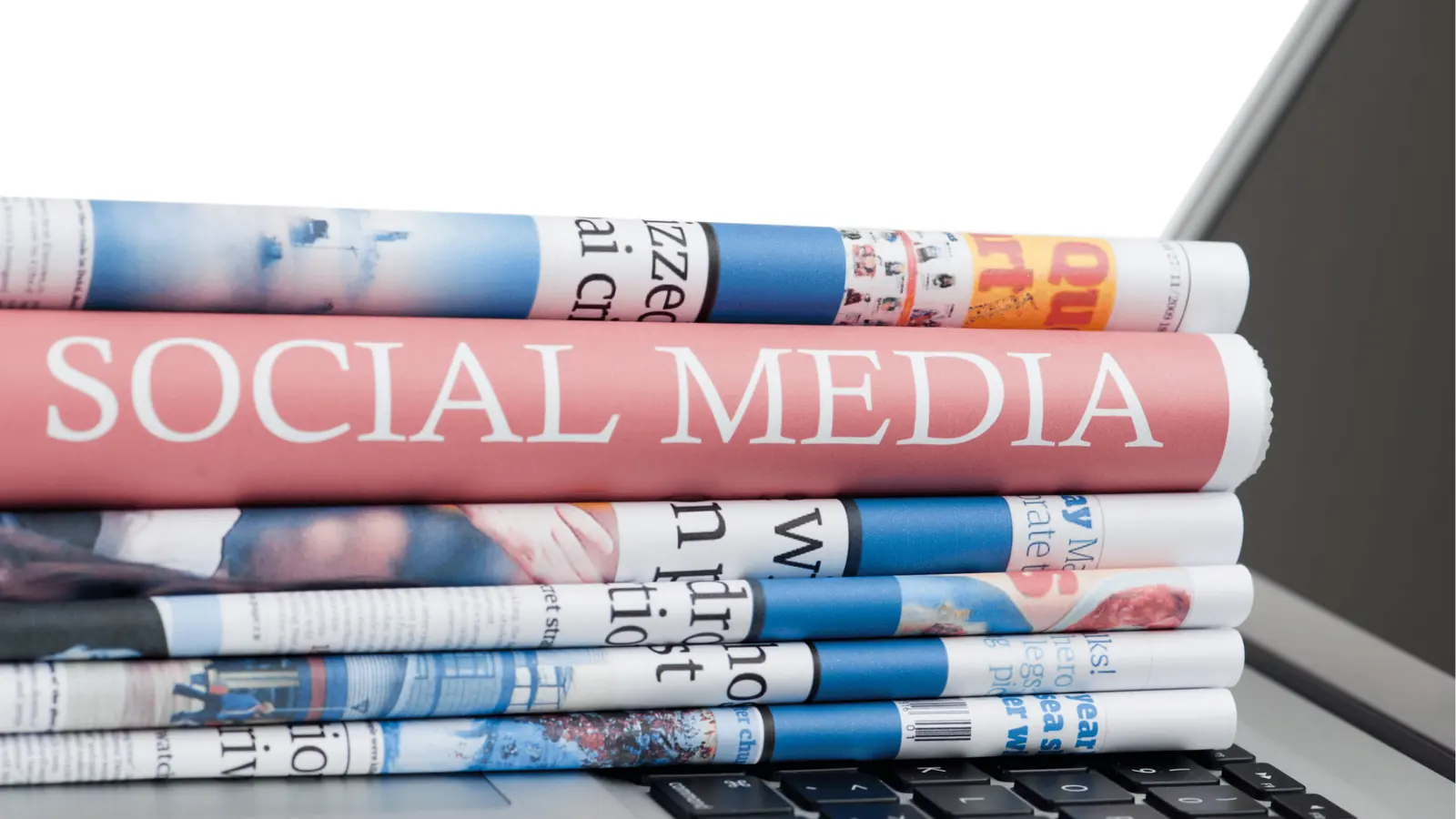 Rolled newspapers stacked on a laptop keyboard with 'SOCIAL MEDIA' headline for brand management
