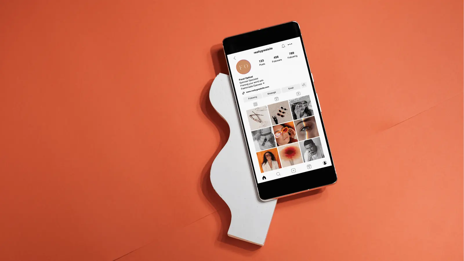 Smartphone displaying an Instagram profile grid on orange background with white prop for content calendar