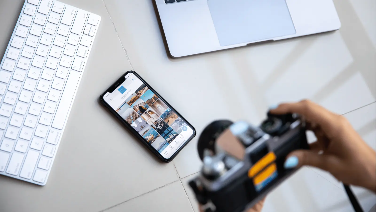 Overhead workspace with smartphone photo gallery, camera, keyboard, and laptop corner