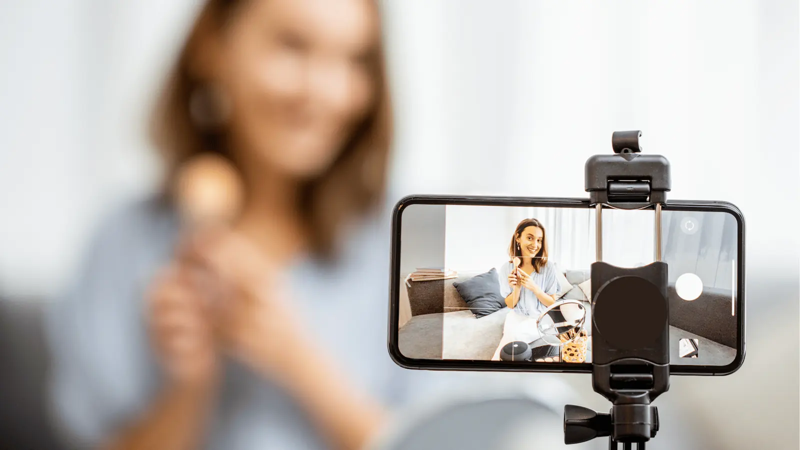 Smartphone on tripod recording a woman doing a makeup tutorial on sofa for brand management