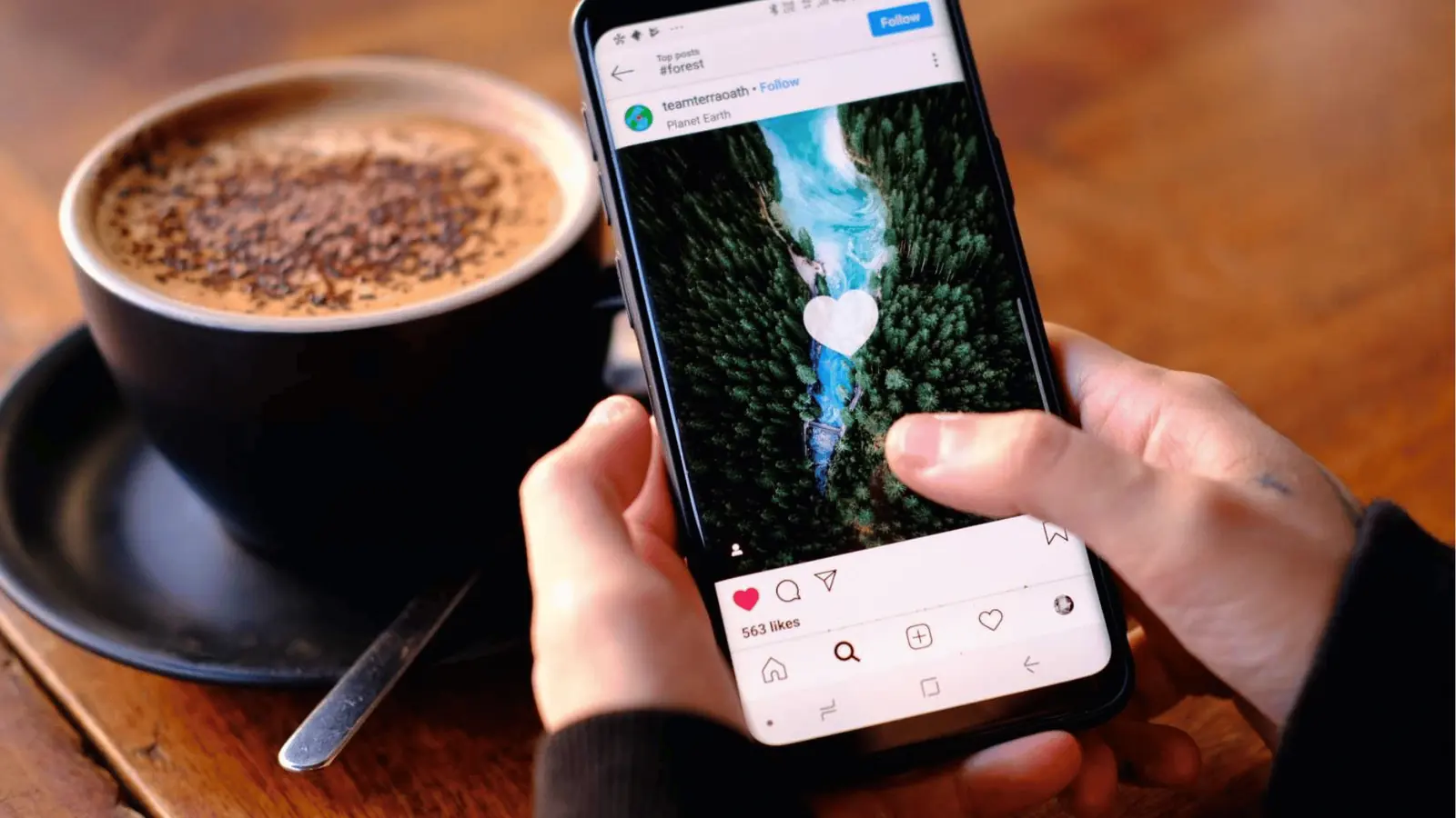 Hands holding a smartphone showing a social media post beside a cup of coffee